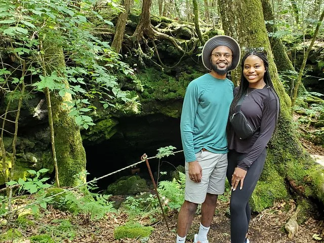 Smiling couple posing near a dark cave entrance in a forest.