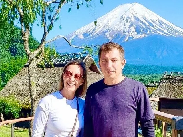 Couple posing with Mount Fuji and traditional thatched-roof houses in the background.