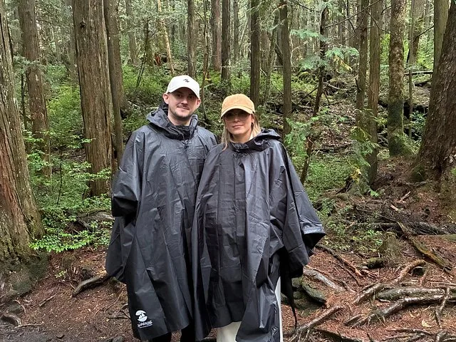 Couple wearing black rain ponchos standing in a dense, green forest.